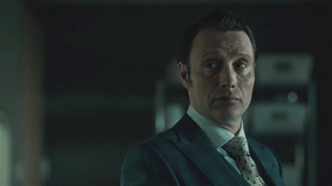 Mads Mikkelsen as Hannibal Lecter, looking away, smirking