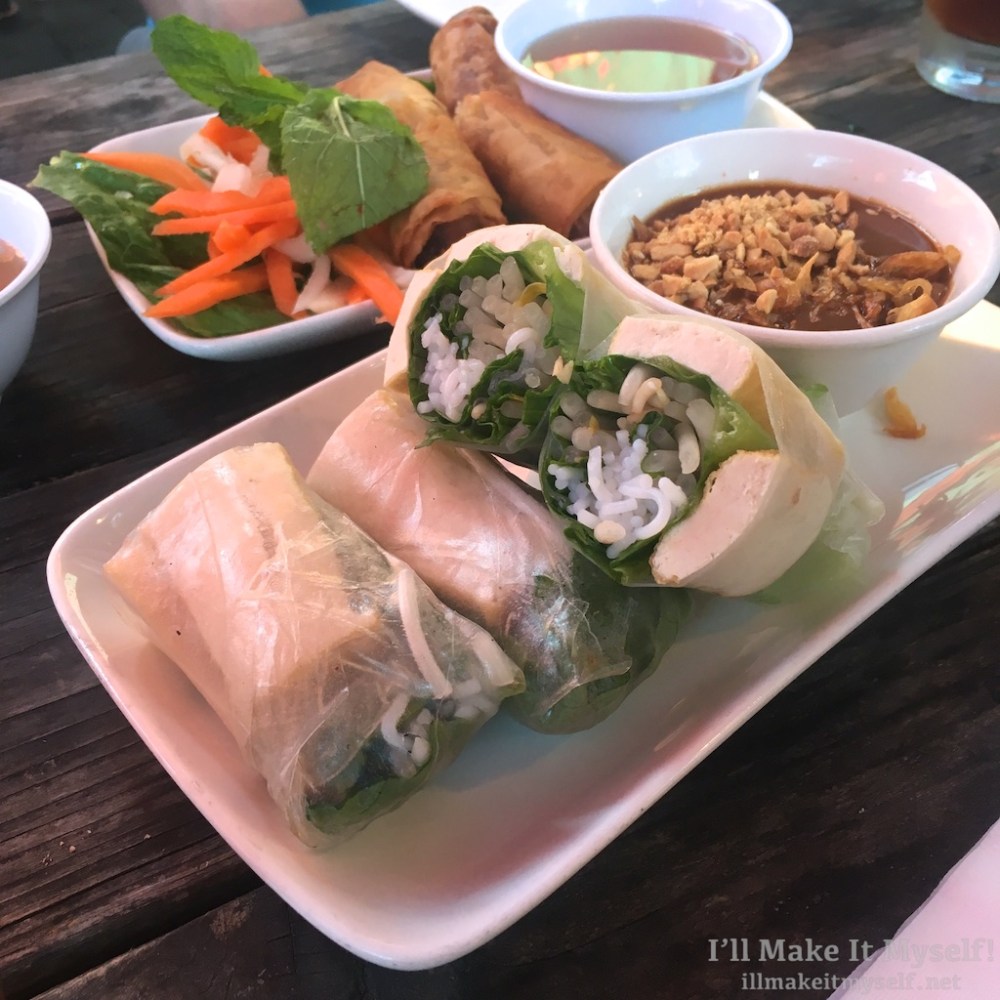 A plate of spring rolls with tofu and peanut sauce on a wooden table.