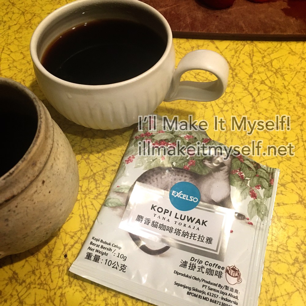 Two clay coffee mugs with an open packet of Kopi Luwak (civet coffee), which has an illustration of a civet (weasel) with a coffee tree.