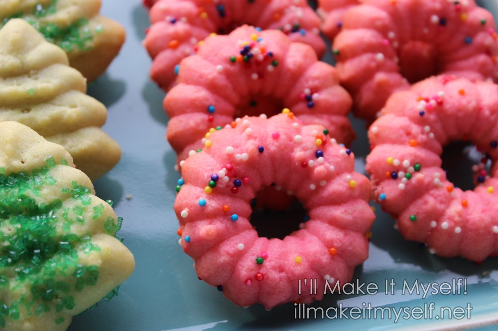 Pink cookies made with the ring plate in the cookie press. They have with rainbow sprinkles to look like doughnuts.