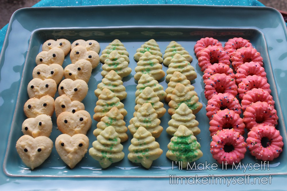 A teal rectangular tray of cookies. There are three kinds of cookies: white heart shapes decorated with black confetti 