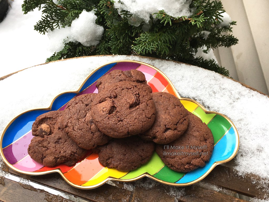 A stack of double-chocolate candy-cane cookies on a rainbow platter on a wooden table covered in snow.