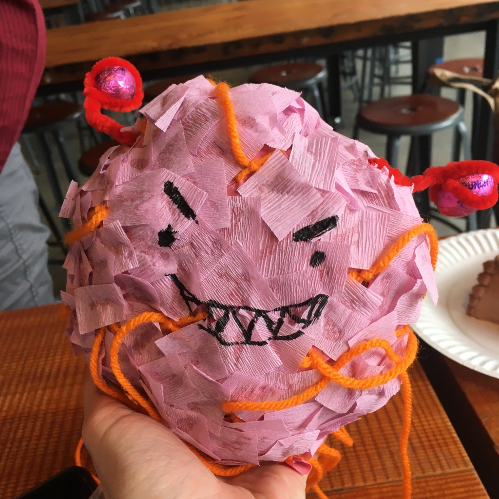 A whoopie cushion covered in pink crepe paper with a sharpied angry smile. There is orange yarn to pull apart the "piñata." The fallopian tubs are red pipecleaners with chocolates wrapped in pink wrappers for the ovaries.